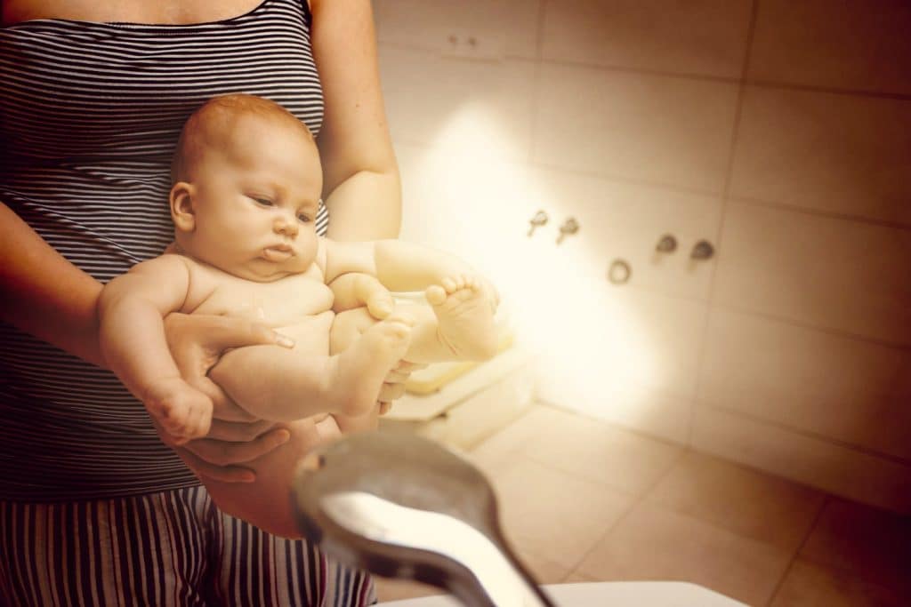 La mère lave son bébé après la selle à la douche